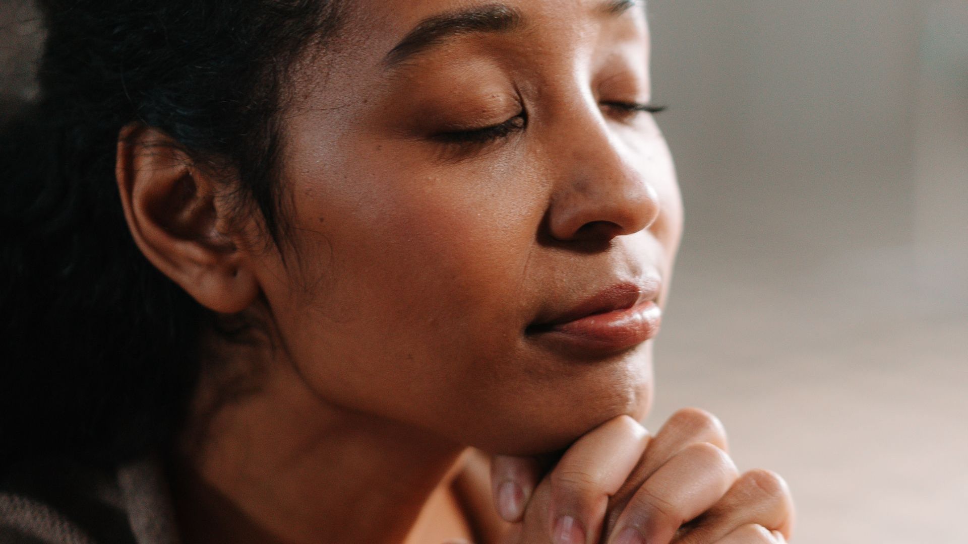 Mulher de olhos fechados, mãos unidas, em tranquila reflexão.