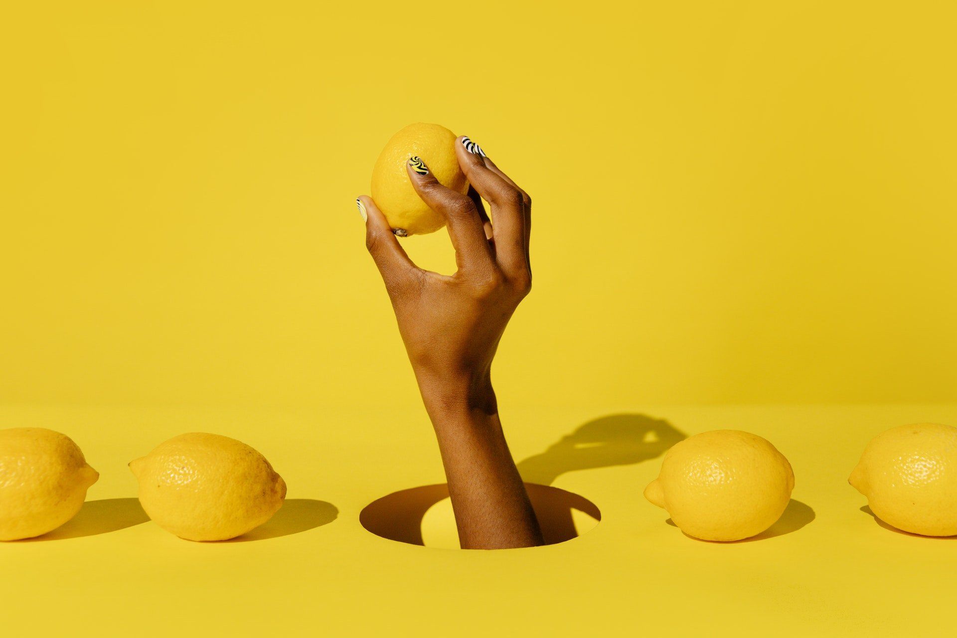 A woman 's hand is sticking out of a hole holding a lemon.
