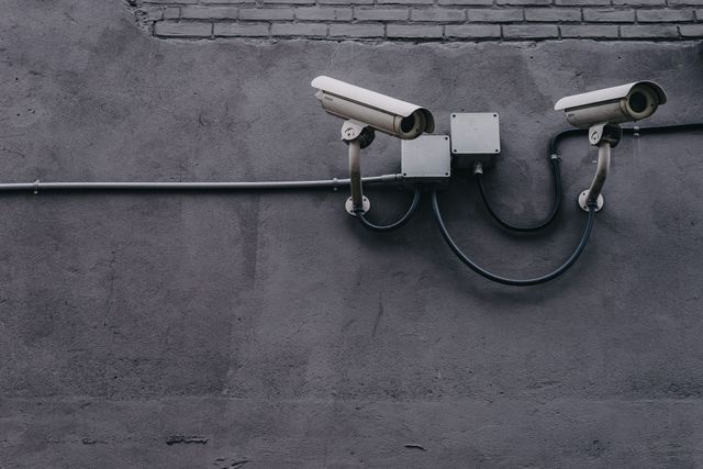 Two security cameras mounted on a gray concrete wall with exposed cables