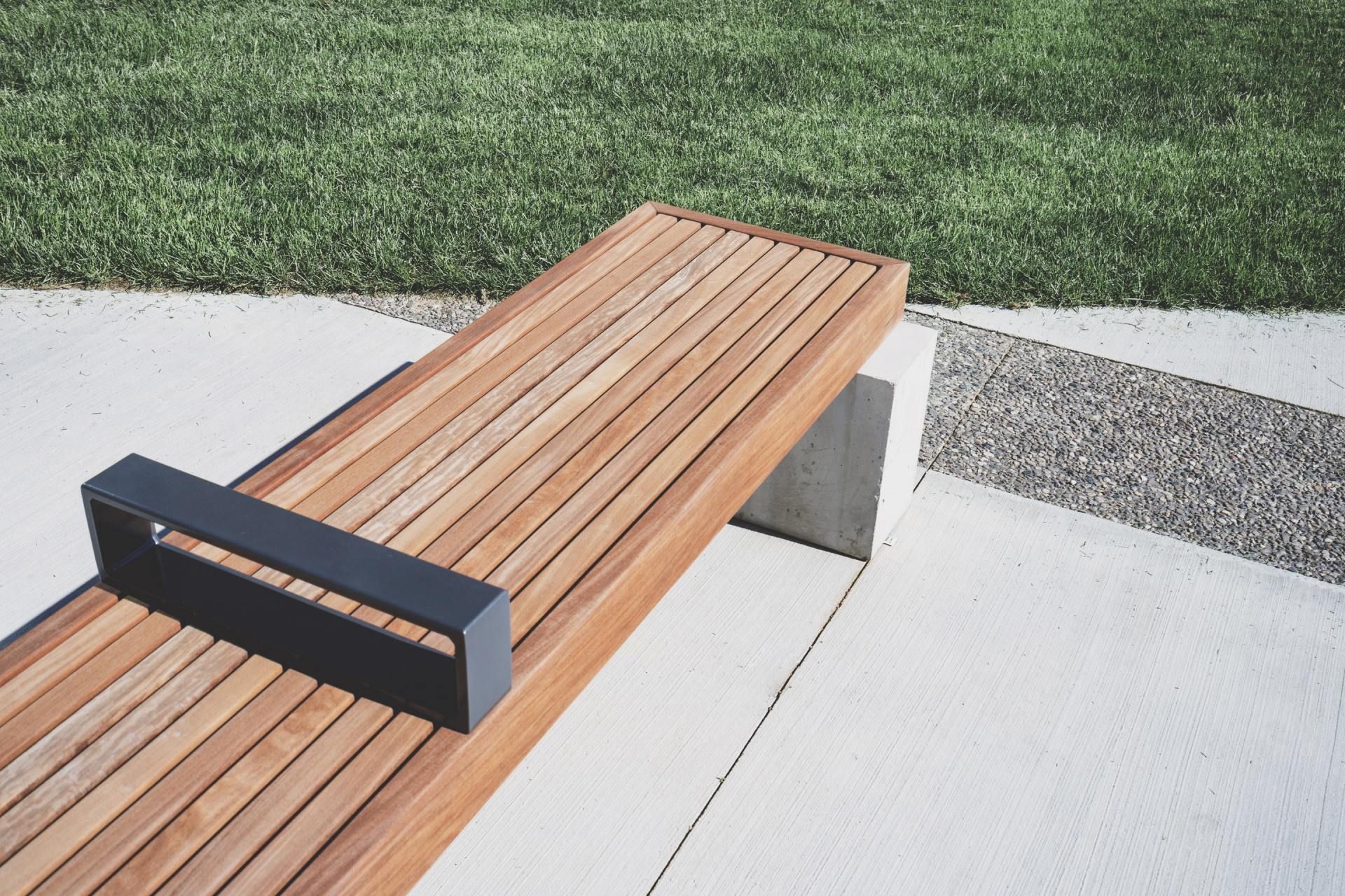 Modern wooden bench with black metal ends beside a concrete path and grass