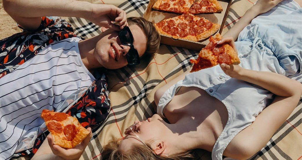 Couple lying on blanket, eating pizza at the beach.