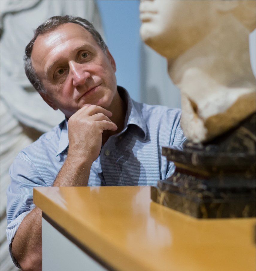 Man examining a sculpture in a museum, blue shirt, thoughtful expression, leaning on a display.