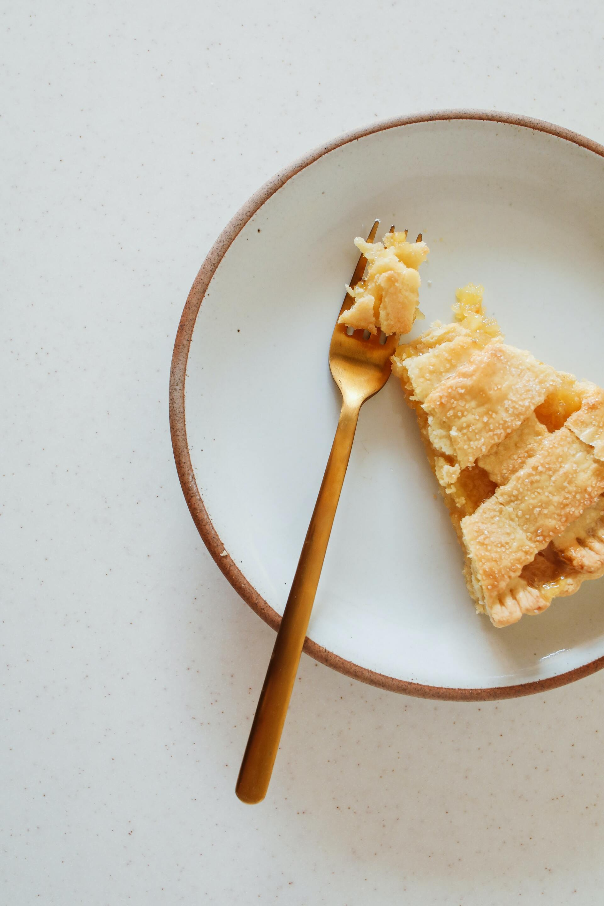 Slice of pie on a white plate with a gold fork; the pie has a lattice crust.