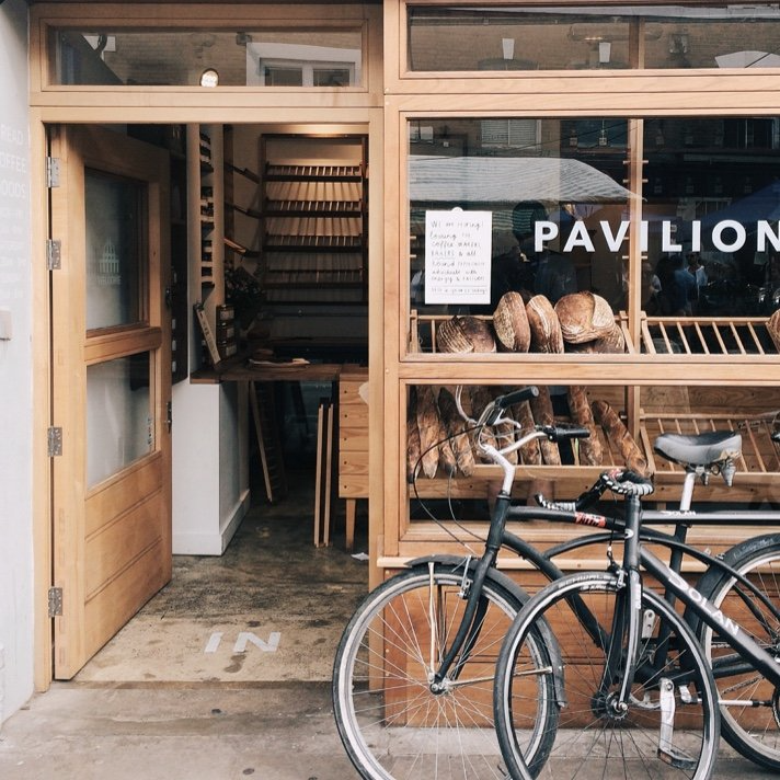 Bakery entrance with open wooden door, display of bread, two bikes parked outside.