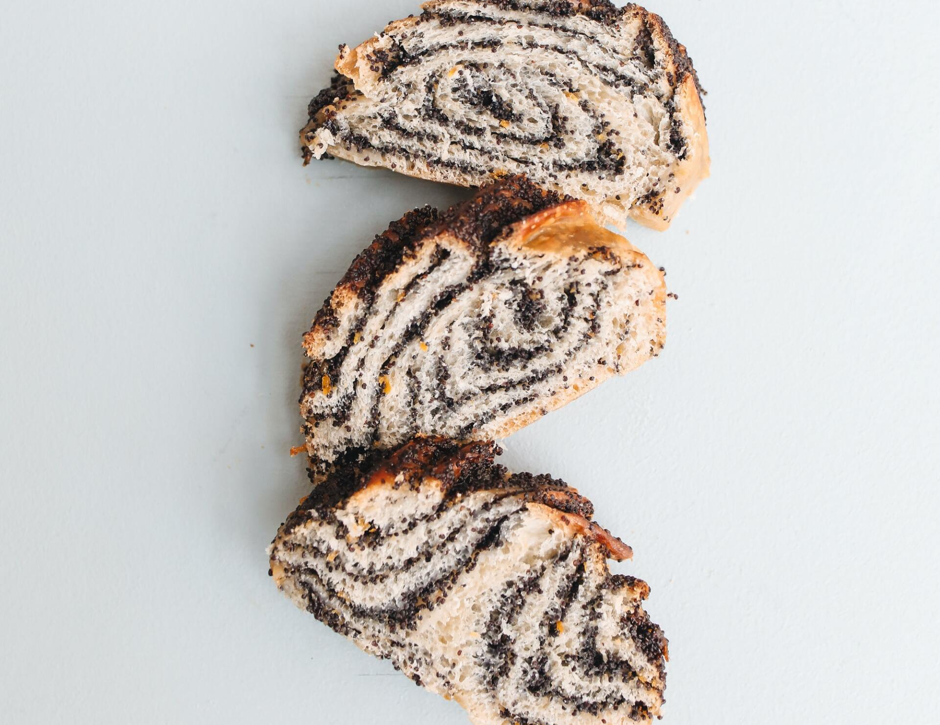Three slices of poppy seed roll on a light blue surface, showing the spiral filling.