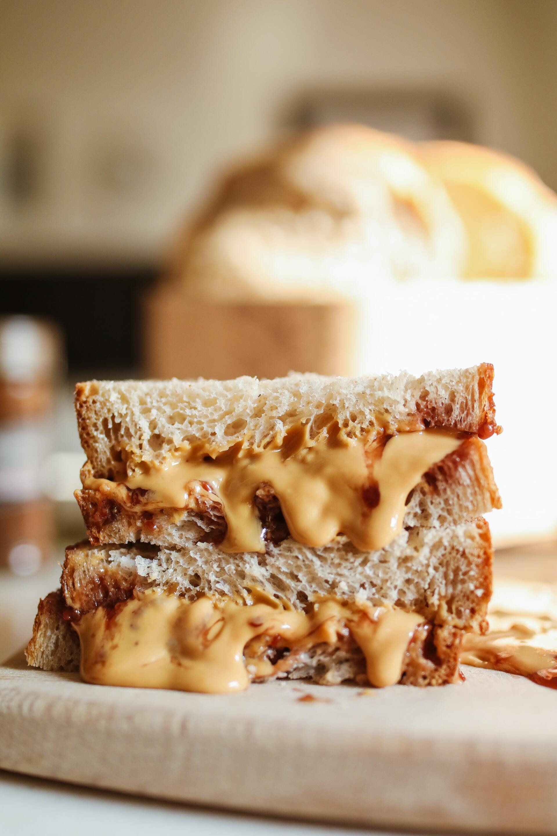 Peanut butter sandwich, cut in half, on a wooden board. Peanut butter oozes from the sides.