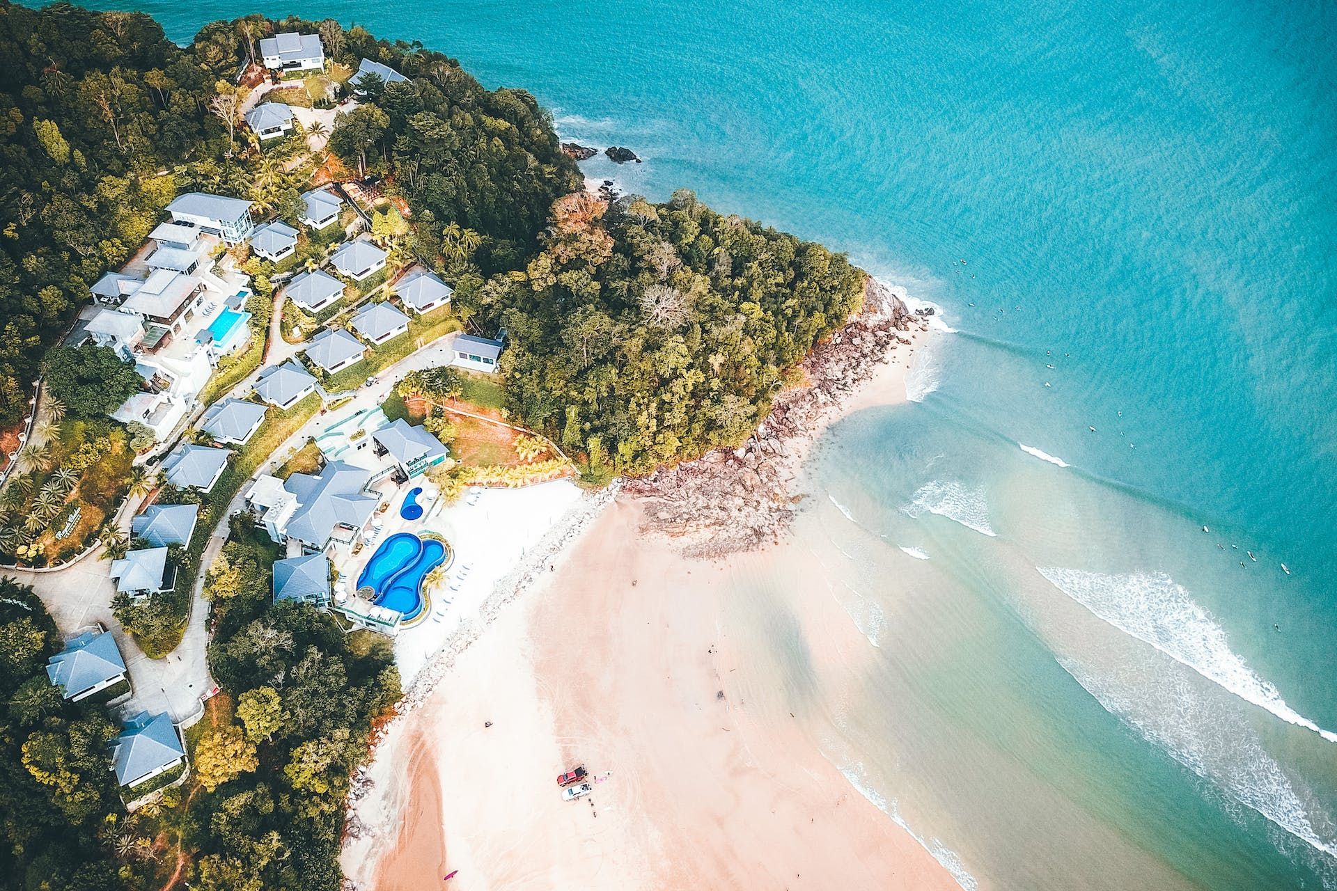 Aerial view of a beach resort with a sandy beach, turquoise water, and lush green forest.