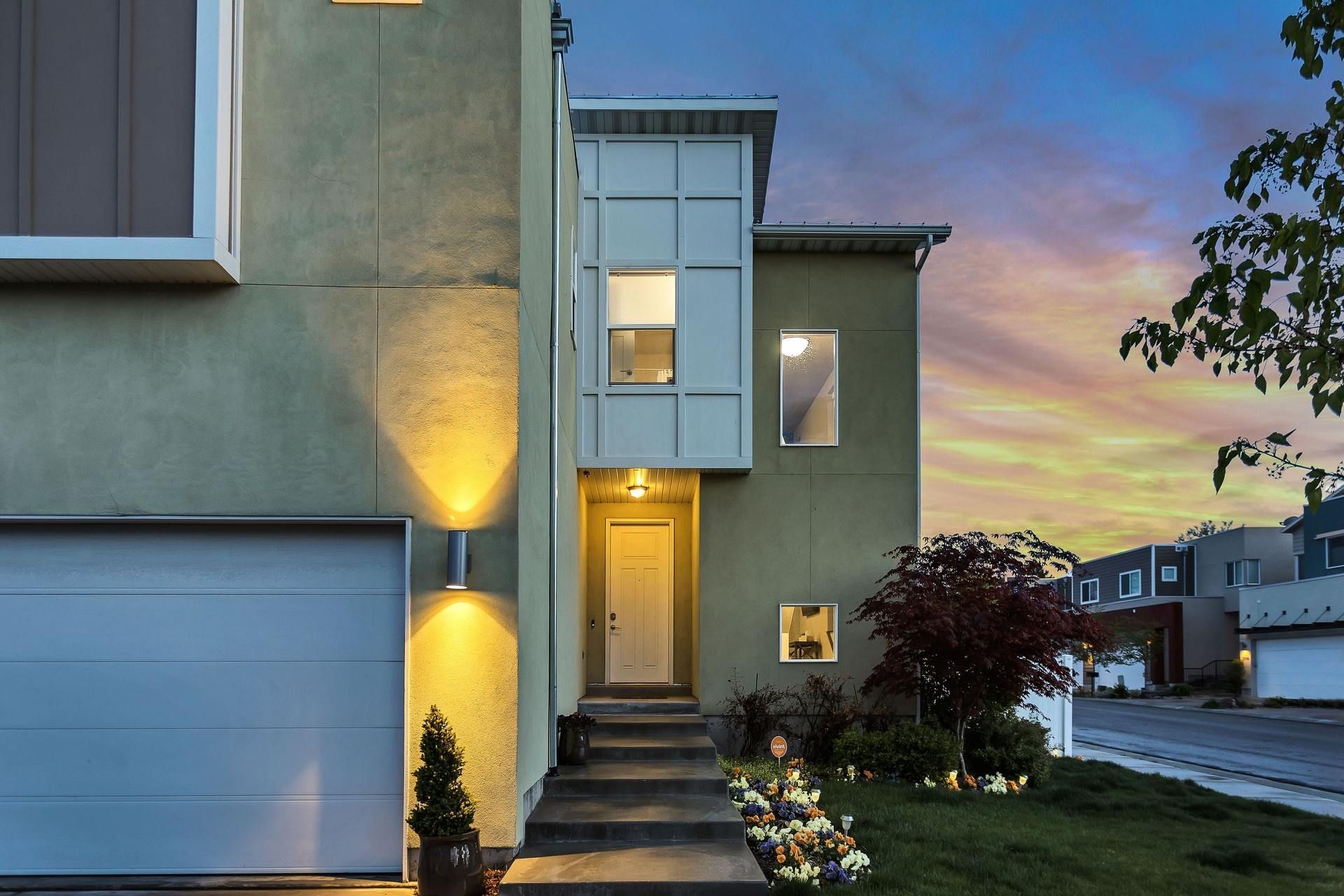 Modern townhouse exterior at dusk with lit entry steps and landscaped front yard.
