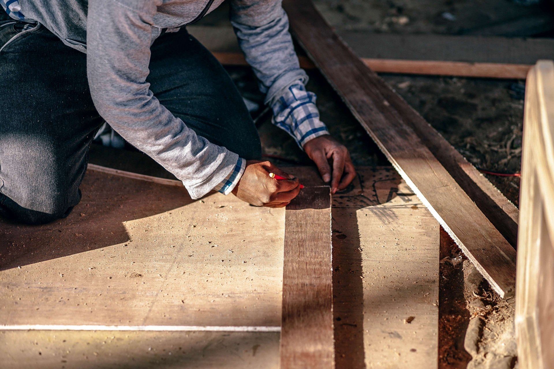 Person measuring and marking a wooden board with a pencil in a workshop.