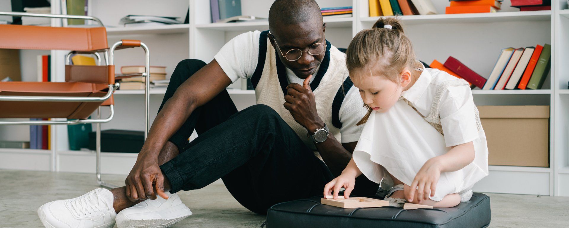 Man and child seated on floor, working on project, books in the background.