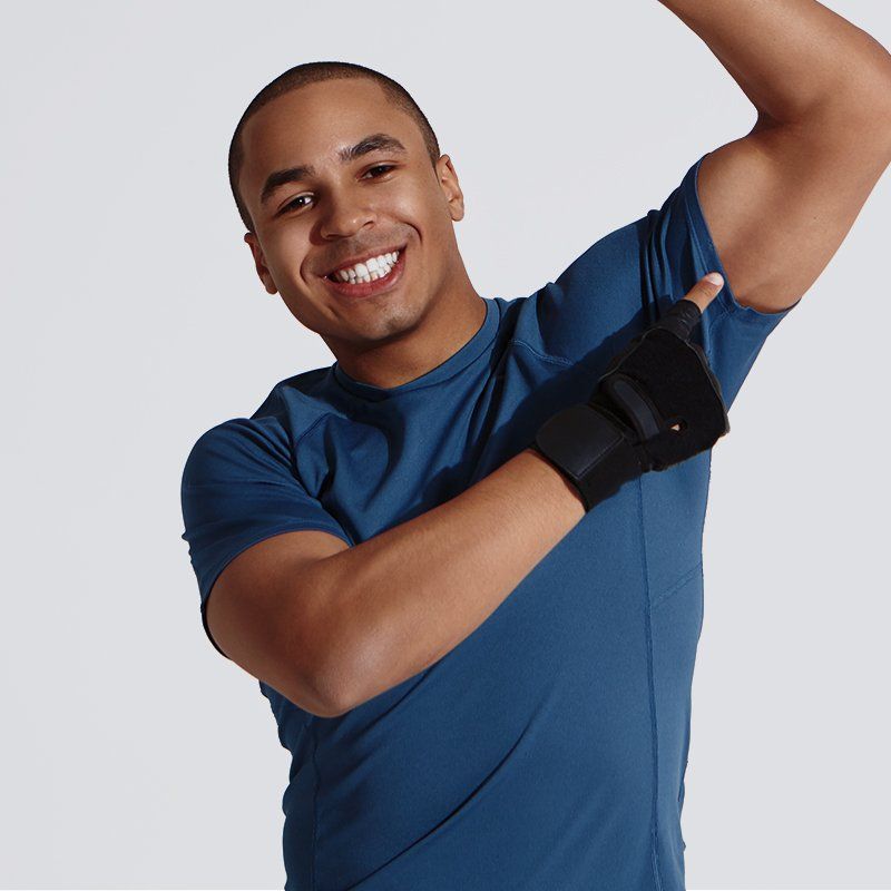 Man in blue shirt, flexing bicep, wearing black wrist support, smiling.