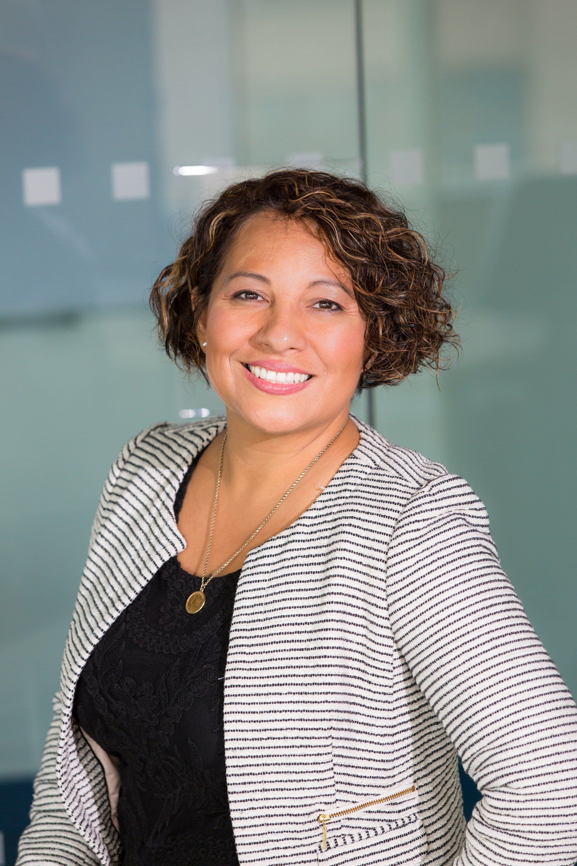 A woman wearing a black shirt and a white jacket is smiling for the camera.