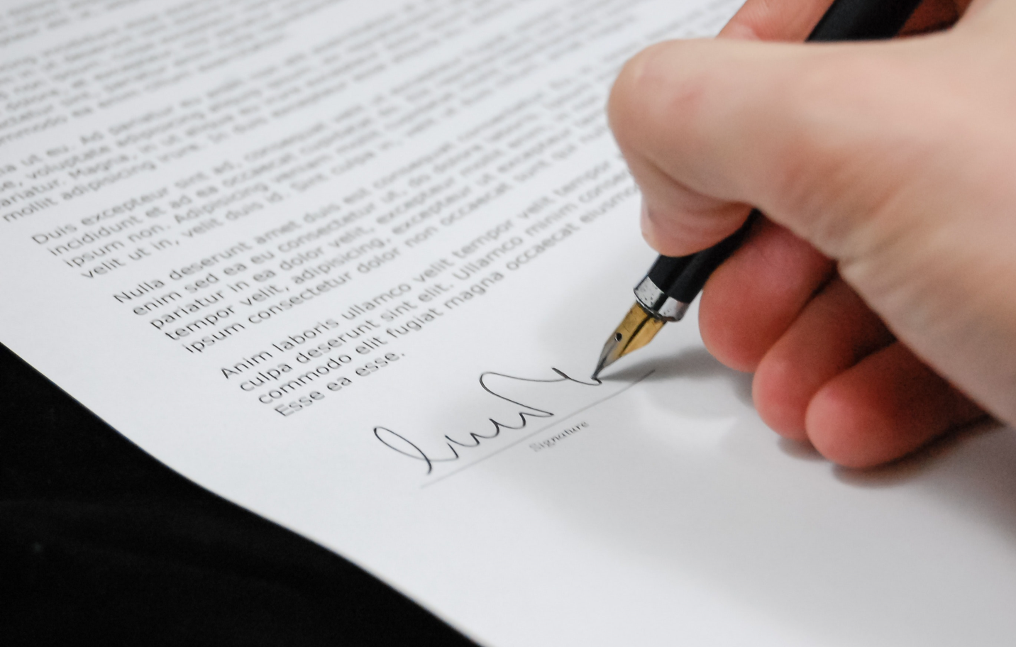 Hand mit Stift, die ein Dokument unterschreibt. Schwarzer Stift schreibt auf weißem Papier.