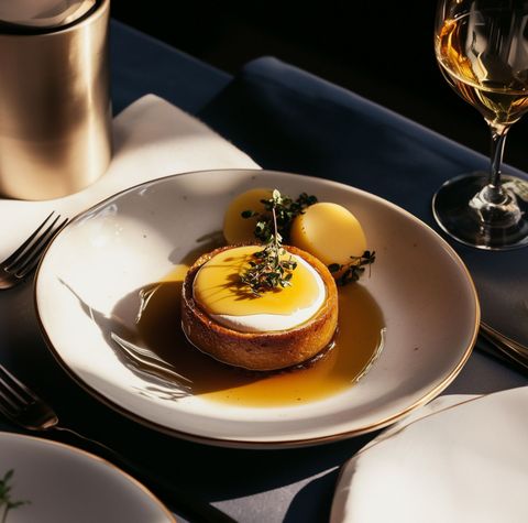 Tarta de postre con salsa amarilla en un plato blanco junto a copas de vino bajo la cálida iluminación del restaurante.
