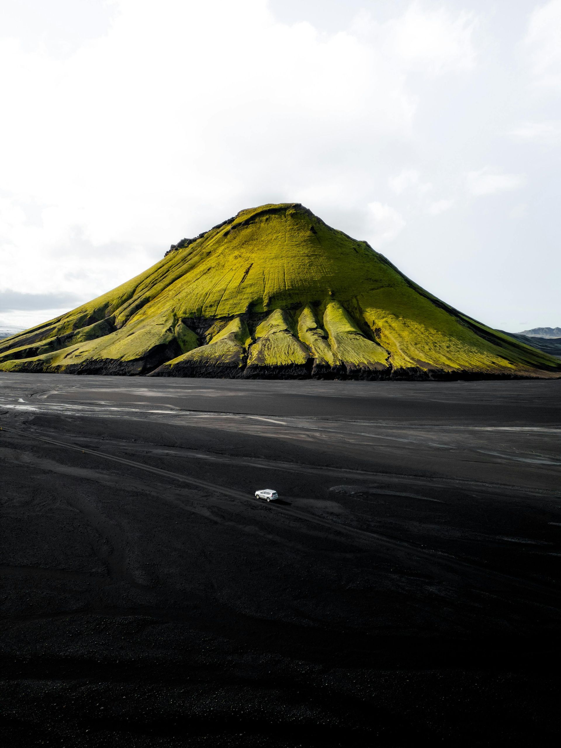 Green mountain rising from black sand, under a cloudy sky.