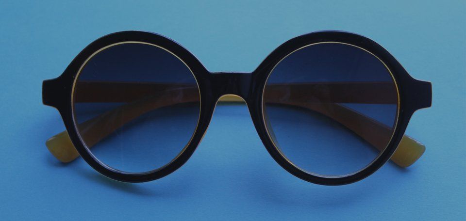 A pair of round sunglasses are sitting on a blue surface.