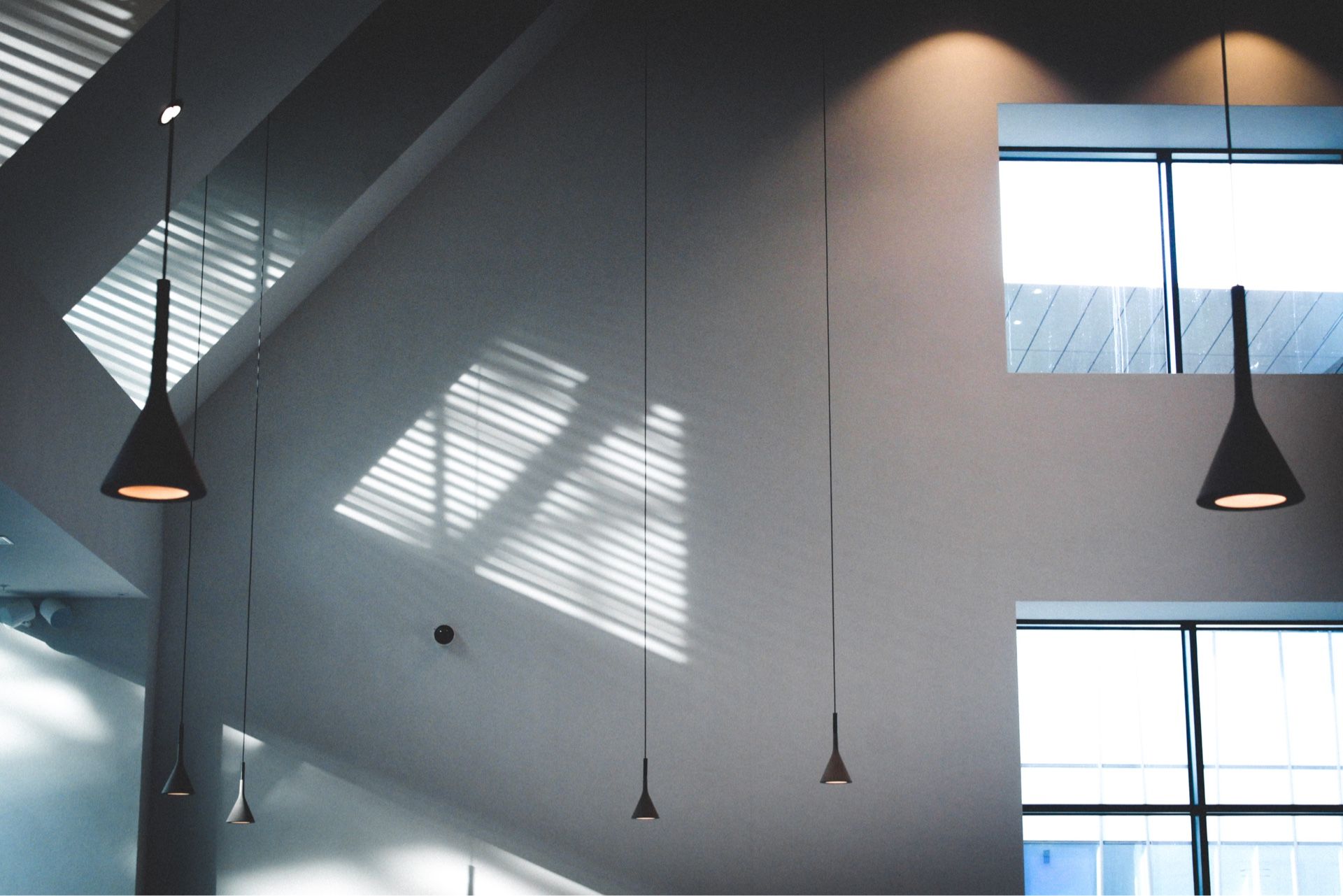 Intérieur moderne avec suspensions lumineuses, une grande fenêtre projetant des ombres et une atmosphère lumineuse et aérée.