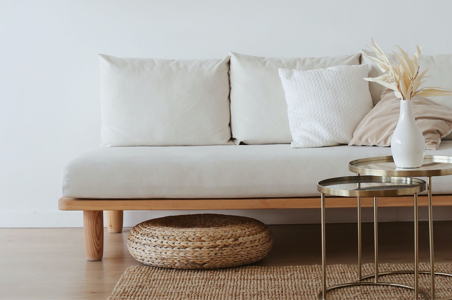 Canapé beige avec coussins, structure en bois et table d'appoint, à côté d'un pouf tressé et d'un tapis.