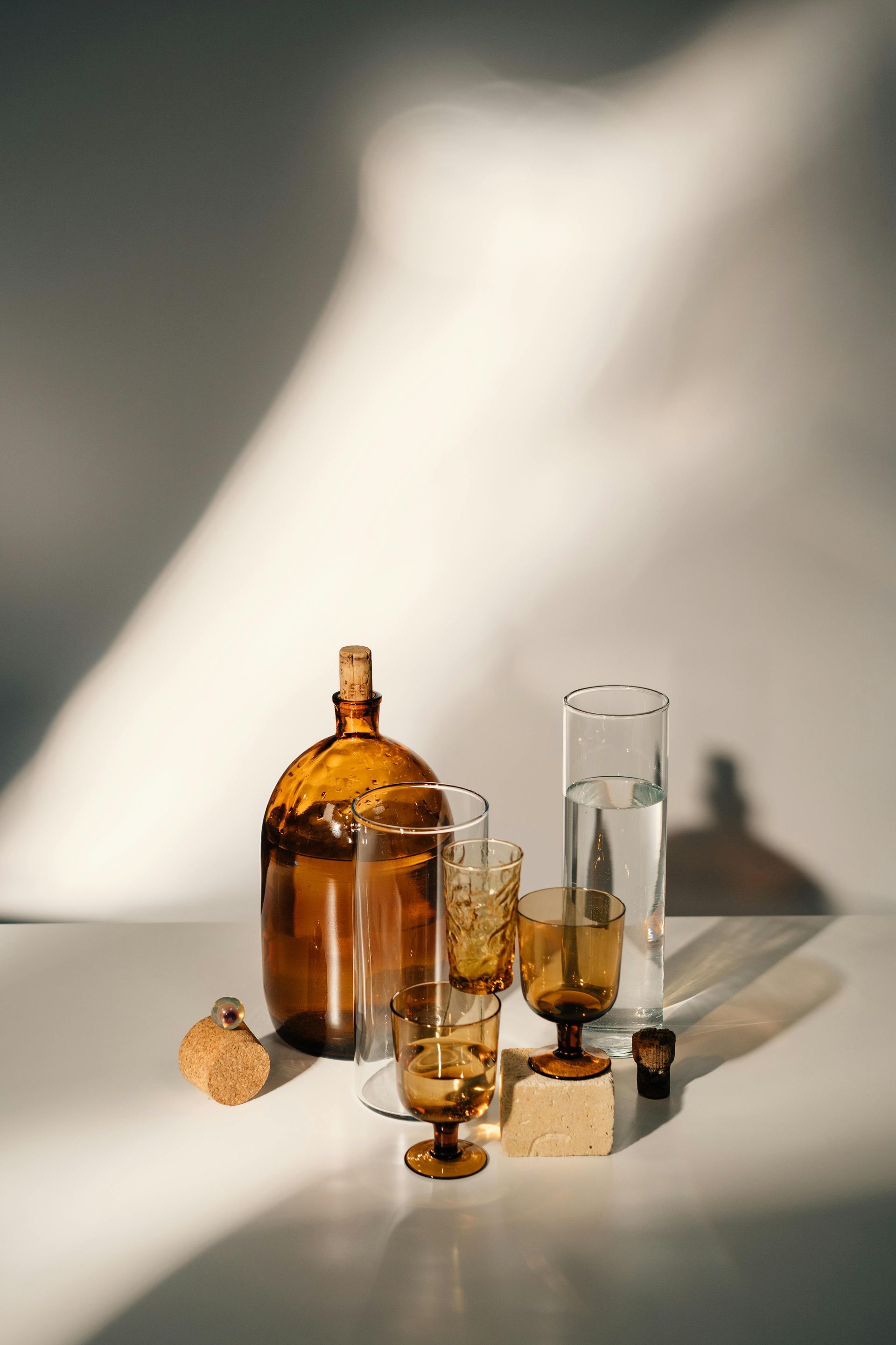 Amber glassware and bottle with corks on a white surface, lit by sunlight.