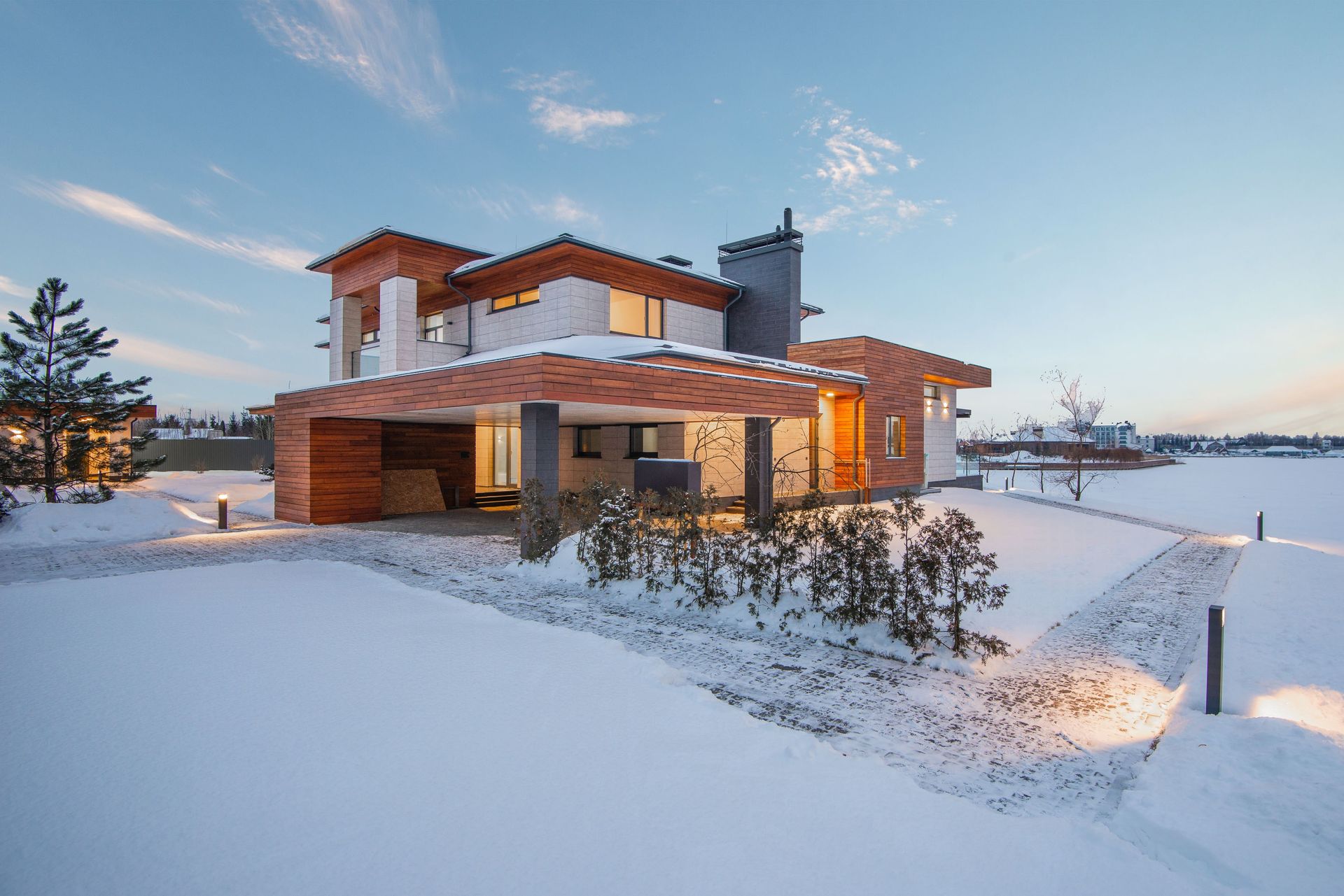 Modern house with wooden facade, snow-covered landscape, evening light.