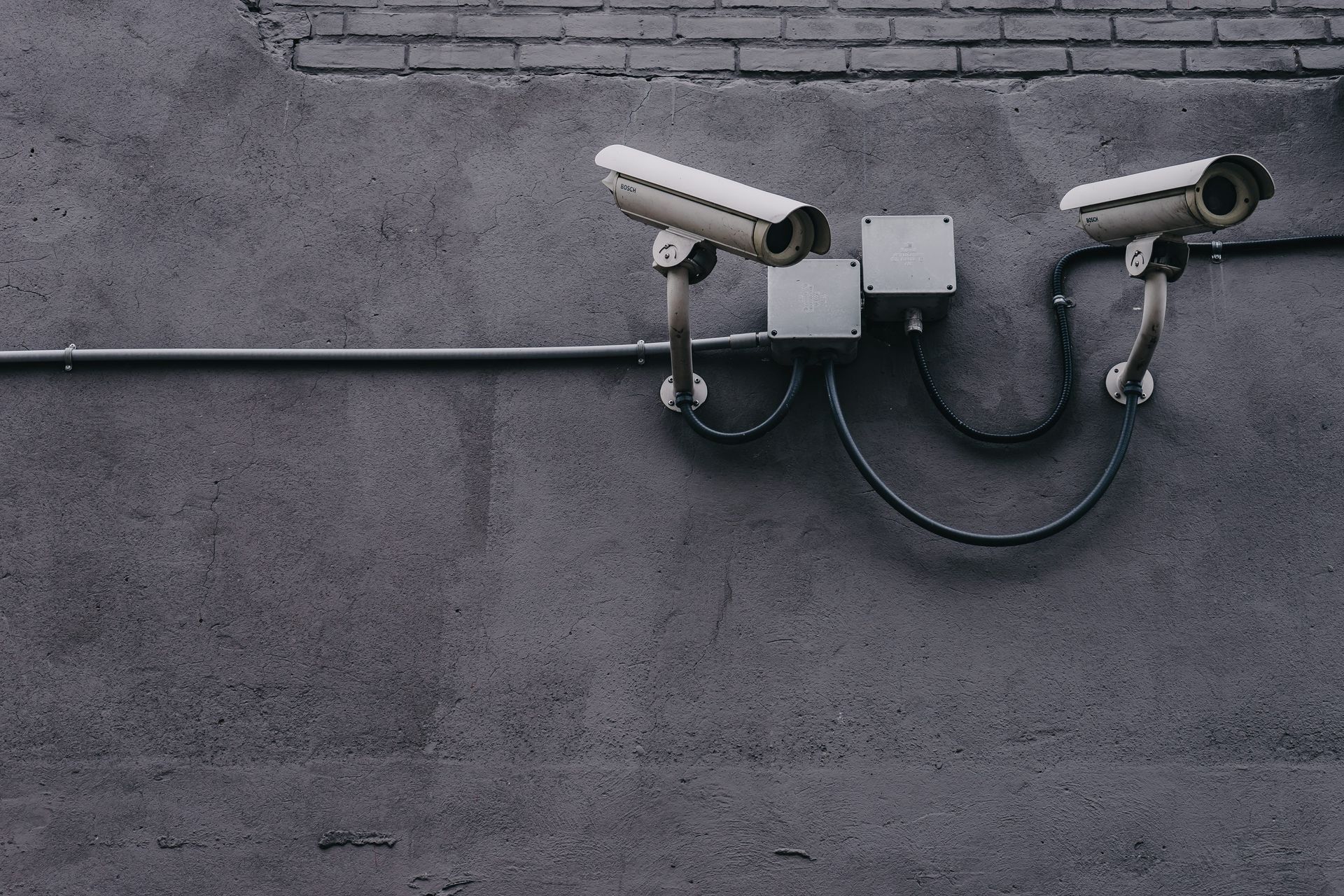 Two security cameras mounted on a gray concrete wall, facing opposite directions.