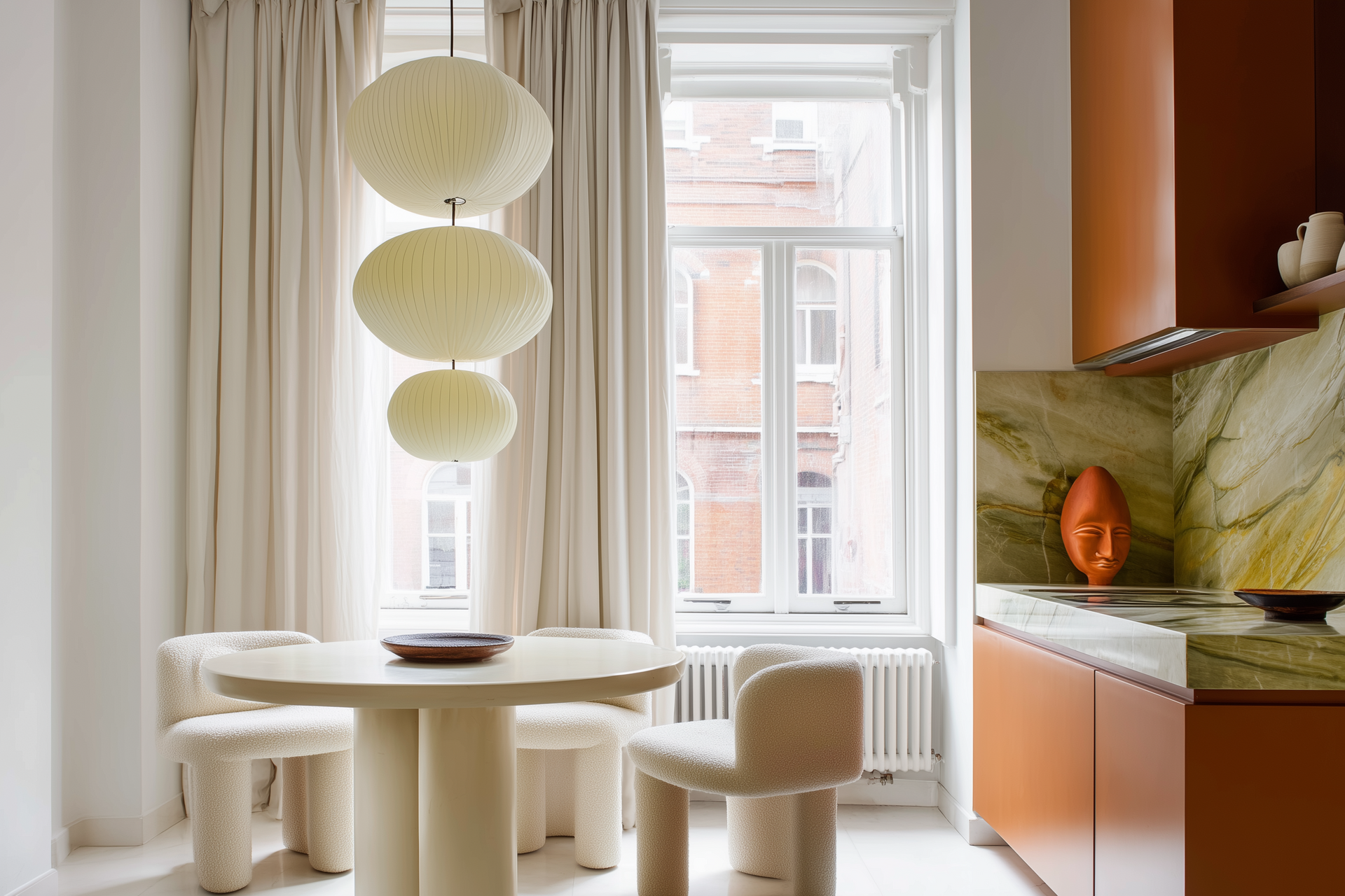 Een kleine, moderne keuken met oranje kastjes, een groene marmeren achterwand, een ronde tafel en hangende bolvormige lampen.