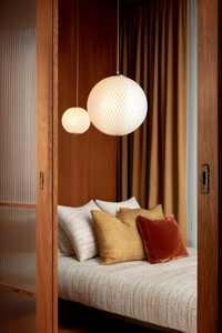 Acogedora habitación con cama, cojines texturizados, paredes de madera cálida y dos lámparas colgantes de globo.