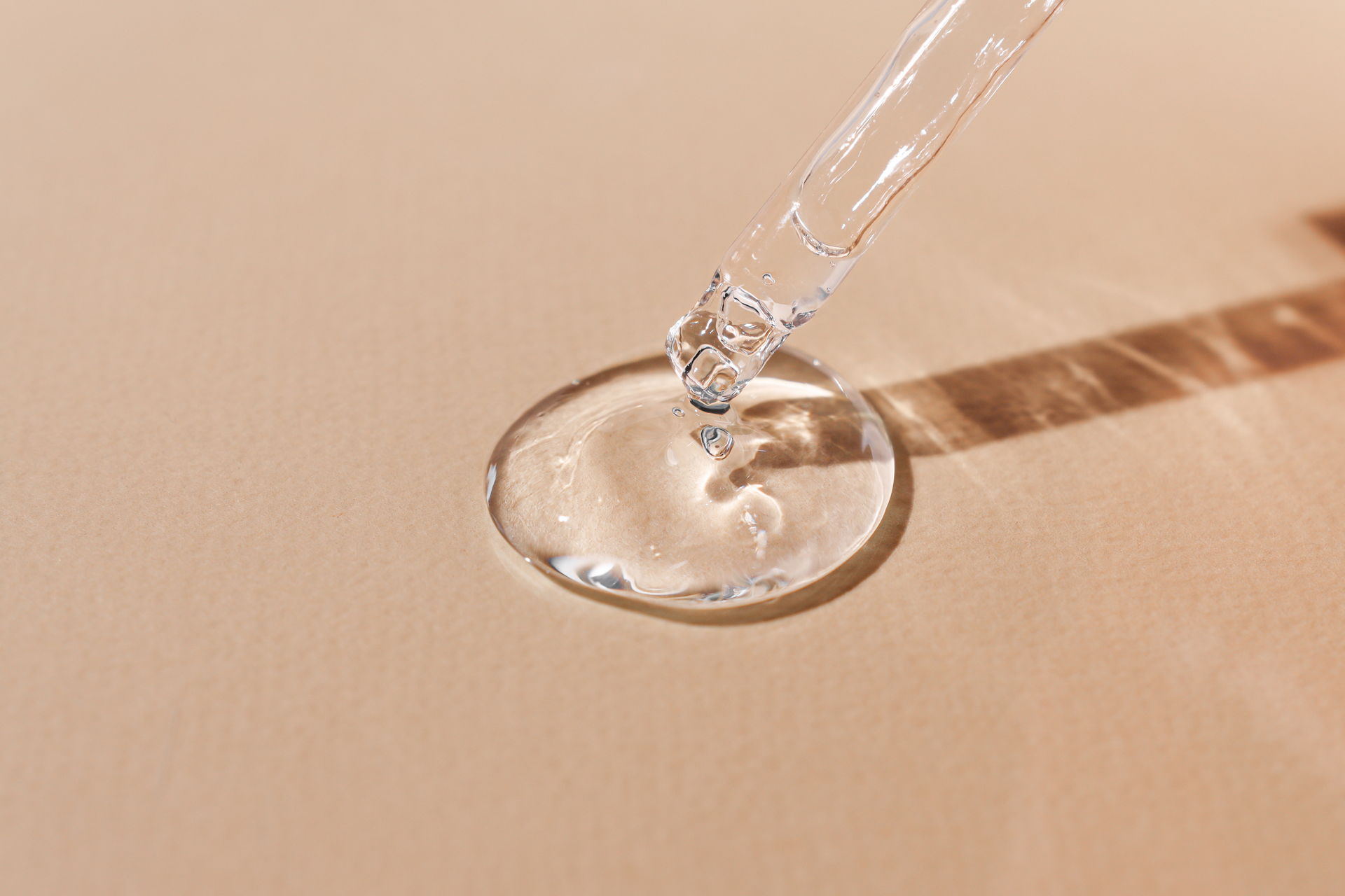 Du sérum transparent s'écoule d'un compte-gouttes sur une surface beige.