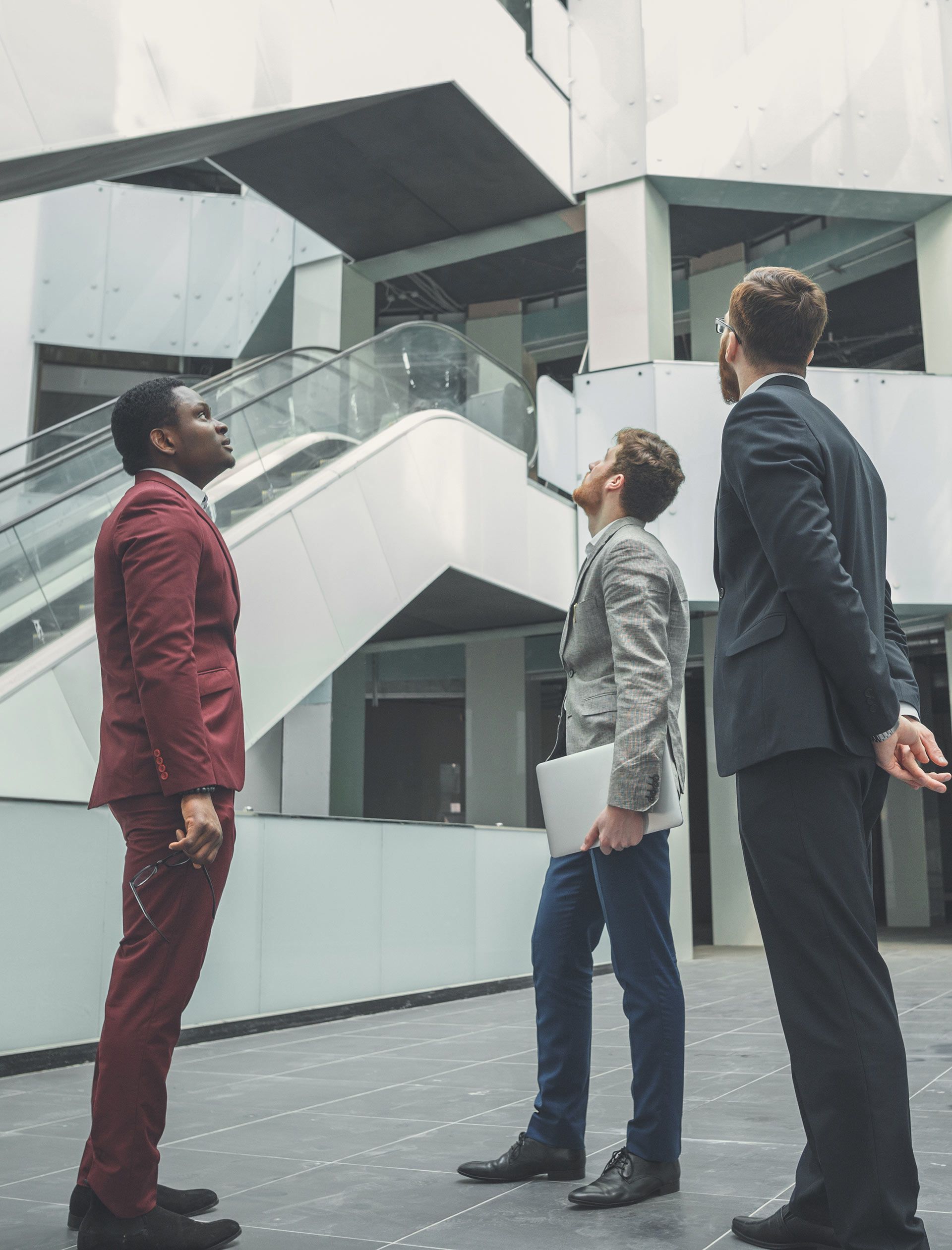 Three people in business attire looking up inside a modern office atrium.