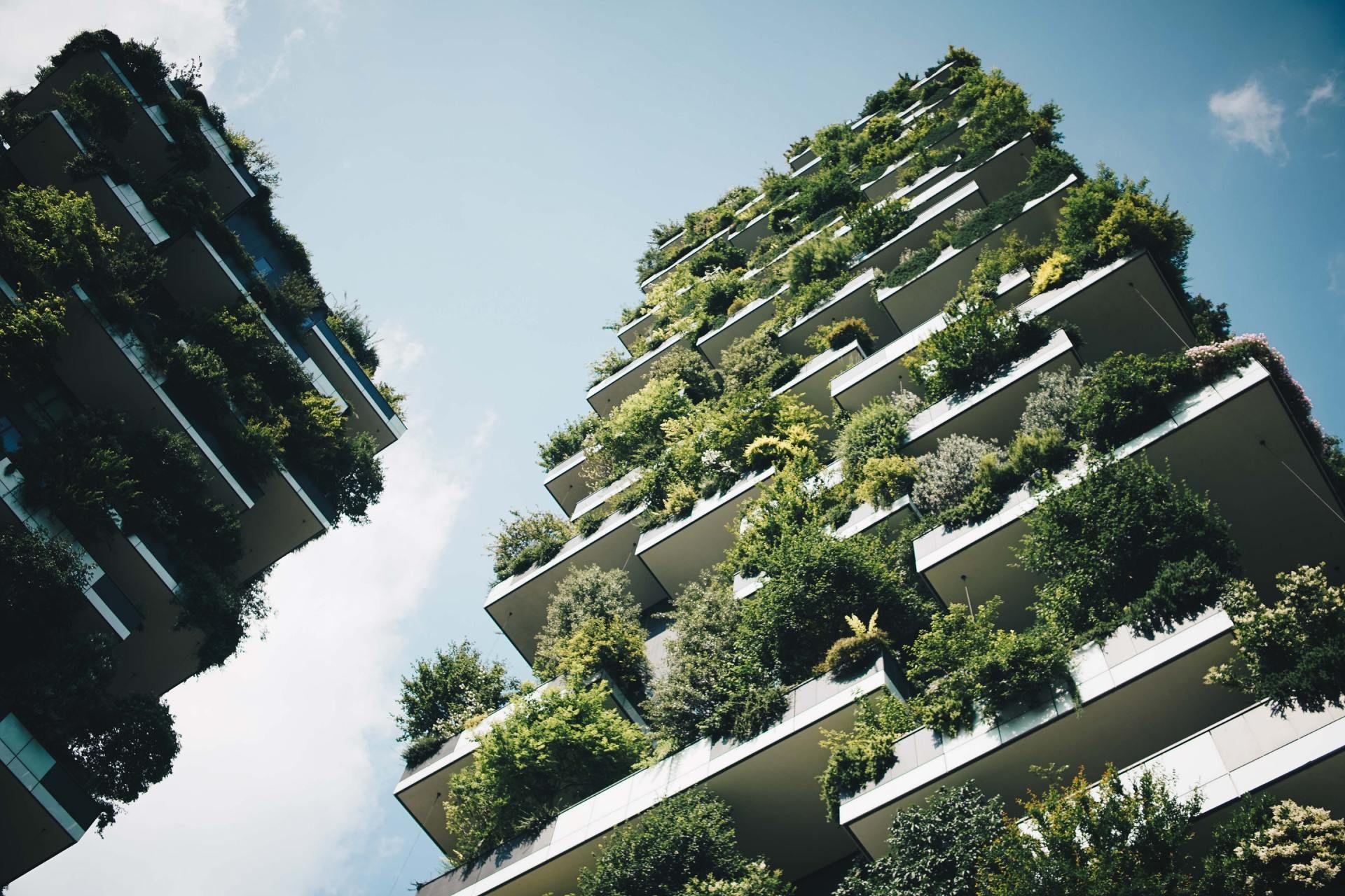 Low-angle view of two modern green-covered high-rise buildings against a bright sky