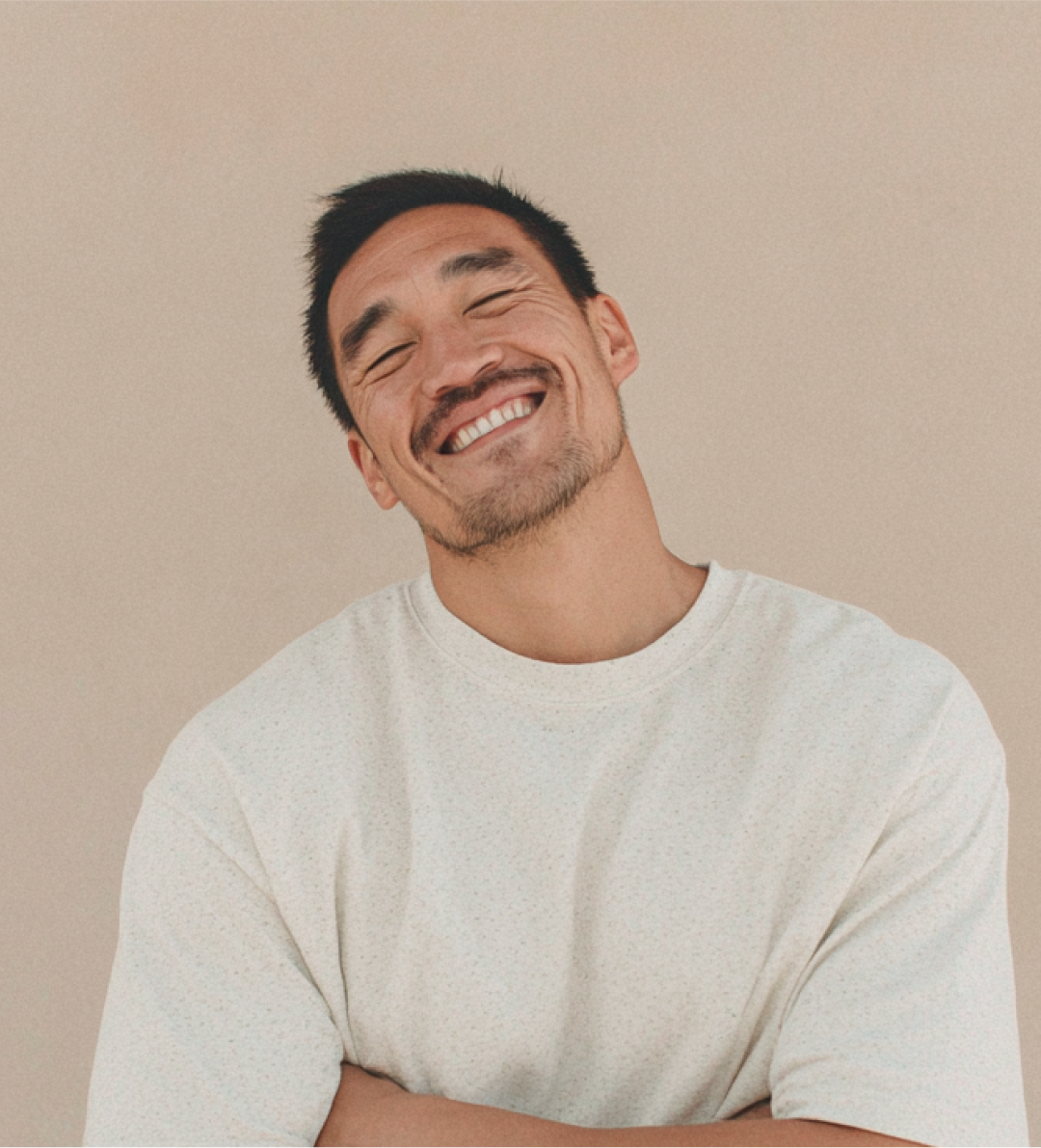 Smiling man in a white shirt against a beige background, head tilted slightly.