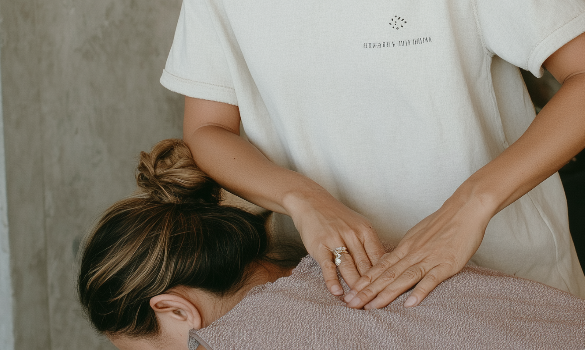 Een massagetherapeut geeft een rugmassage aan een persoon die op zijn buik ligt, bedekt met een doek met textuur, in een spa-omgeving.