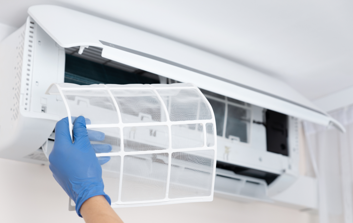 Person in blue gloves removing an air filter from a wall-mounted air conditioning unit.