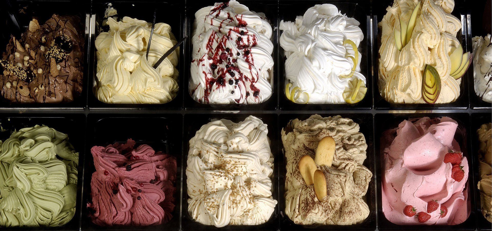 A display case of various colorful gelato flavors arranged in rows.