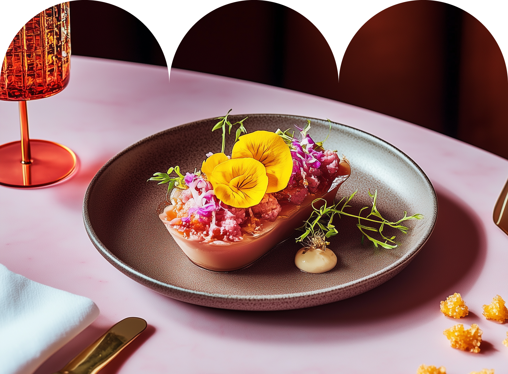 Postre gourmet emplatado con guarnición morada y flores amarillas sobre una mesa rosa.