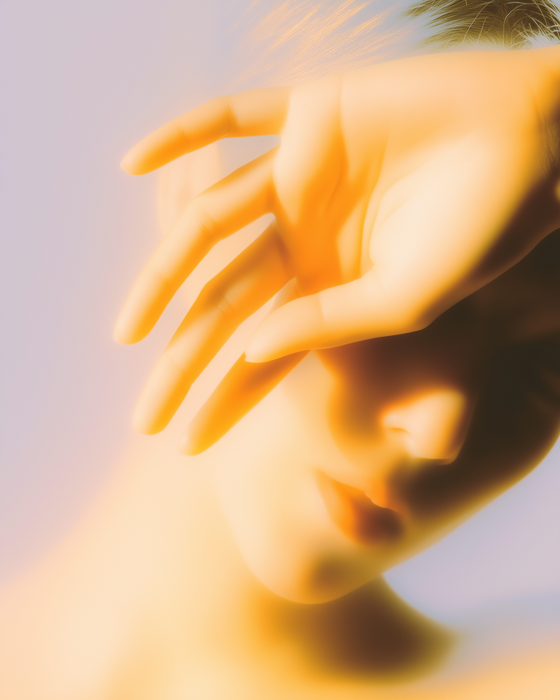 Retrato con enfoque suave de una persona que se cubre el rostro con la mano, bajo una cálida luz dorada.