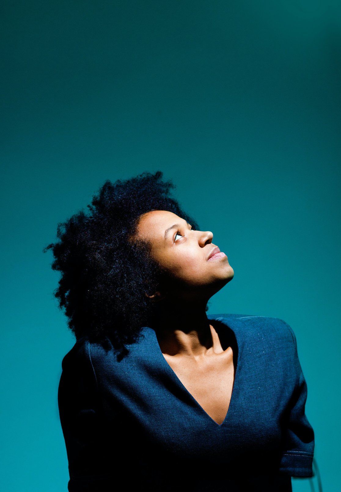 A woman in a blue sweater is looking up at the sky.