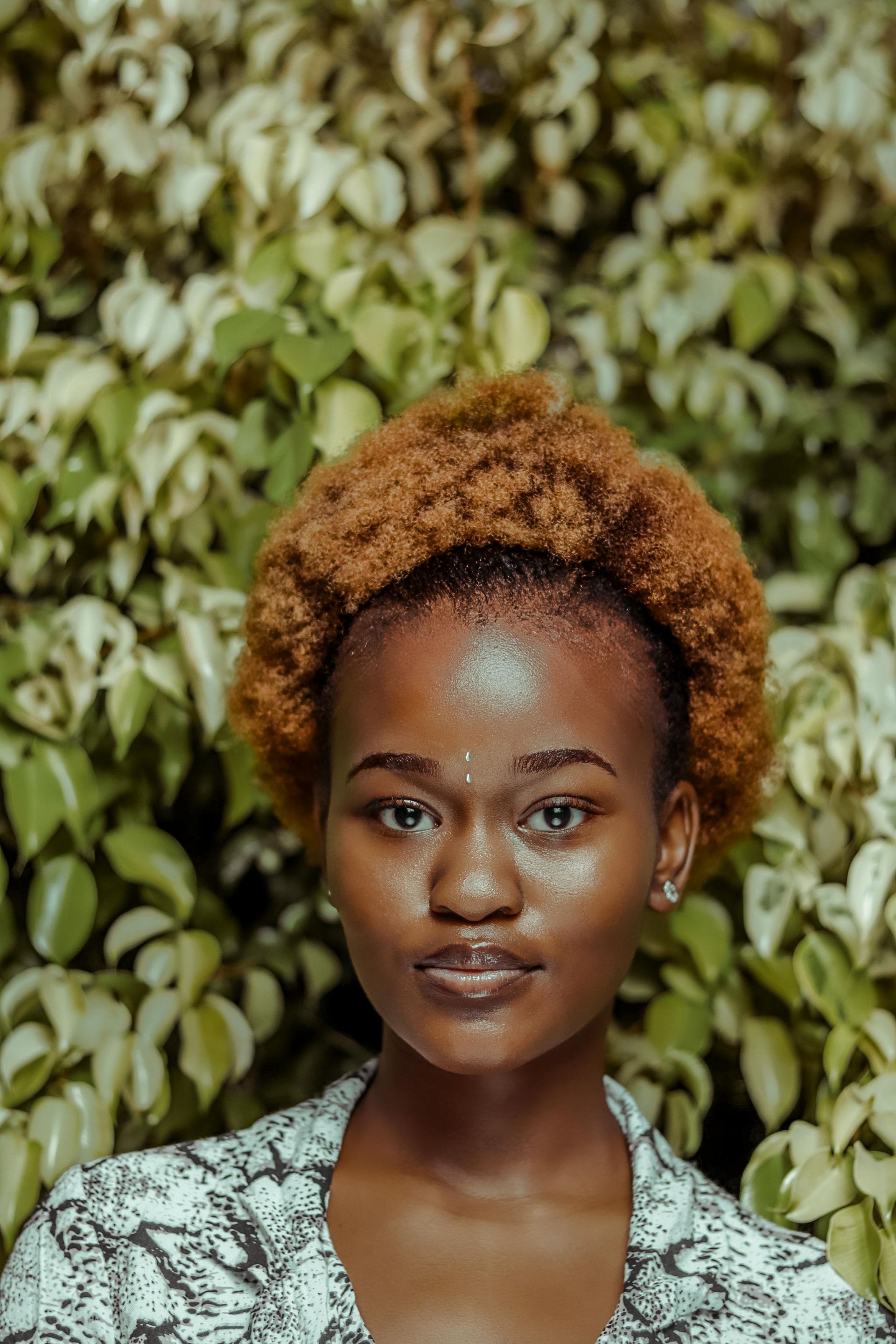 Portrait of a person with curly hair against a leafy green background