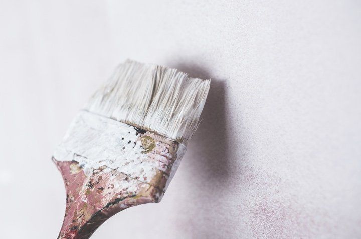 Pincel con cerdas blancas que aplica pintura blanca sobre una pared de color rosa claro.