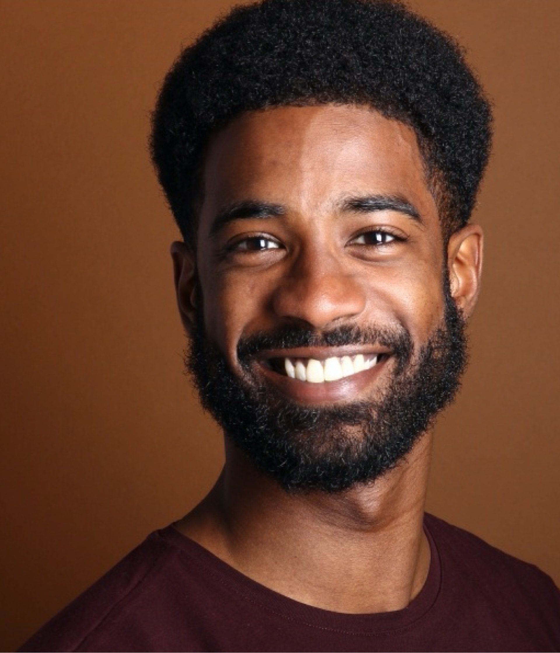 A man with a beard is smiling and wearing a maroon shirt