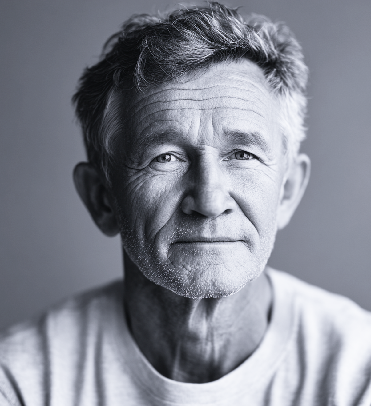 Gray-scale portrait of an older man with a neutral expression, light hair, and a white t-shirt.
