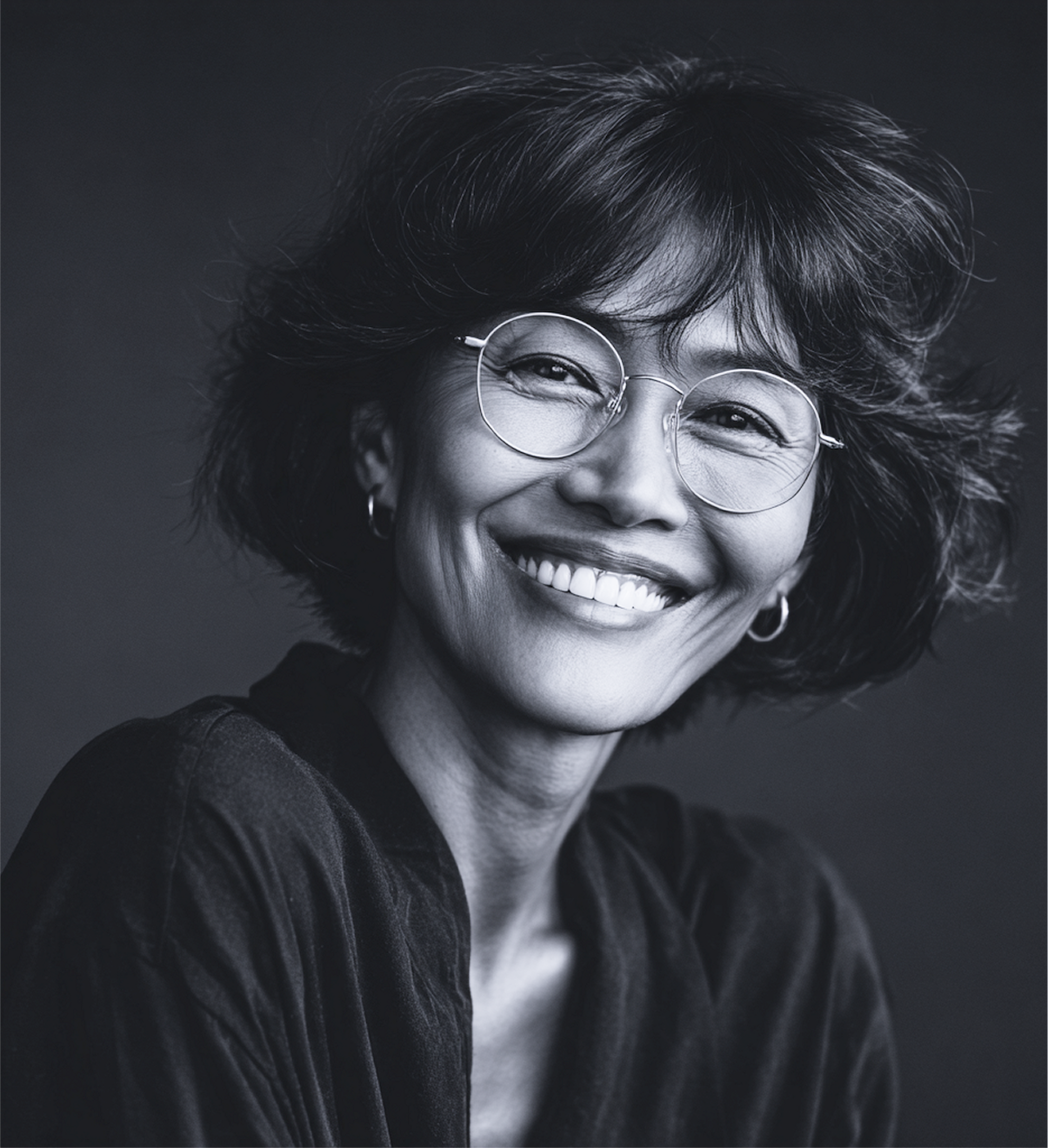 Woman with glasses smiles broadly, dark hair, wearing a dark shirt. Black and white photo.