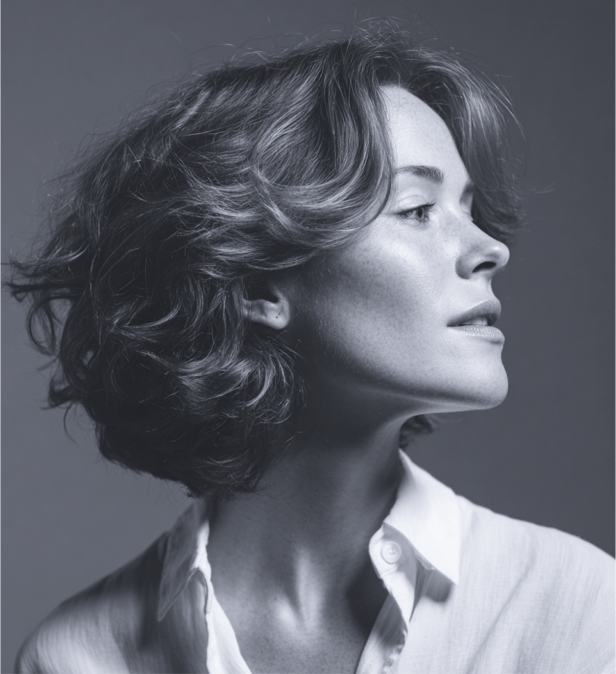 Woman with short, wavy hair, looking right, wearing a white collared shirt.