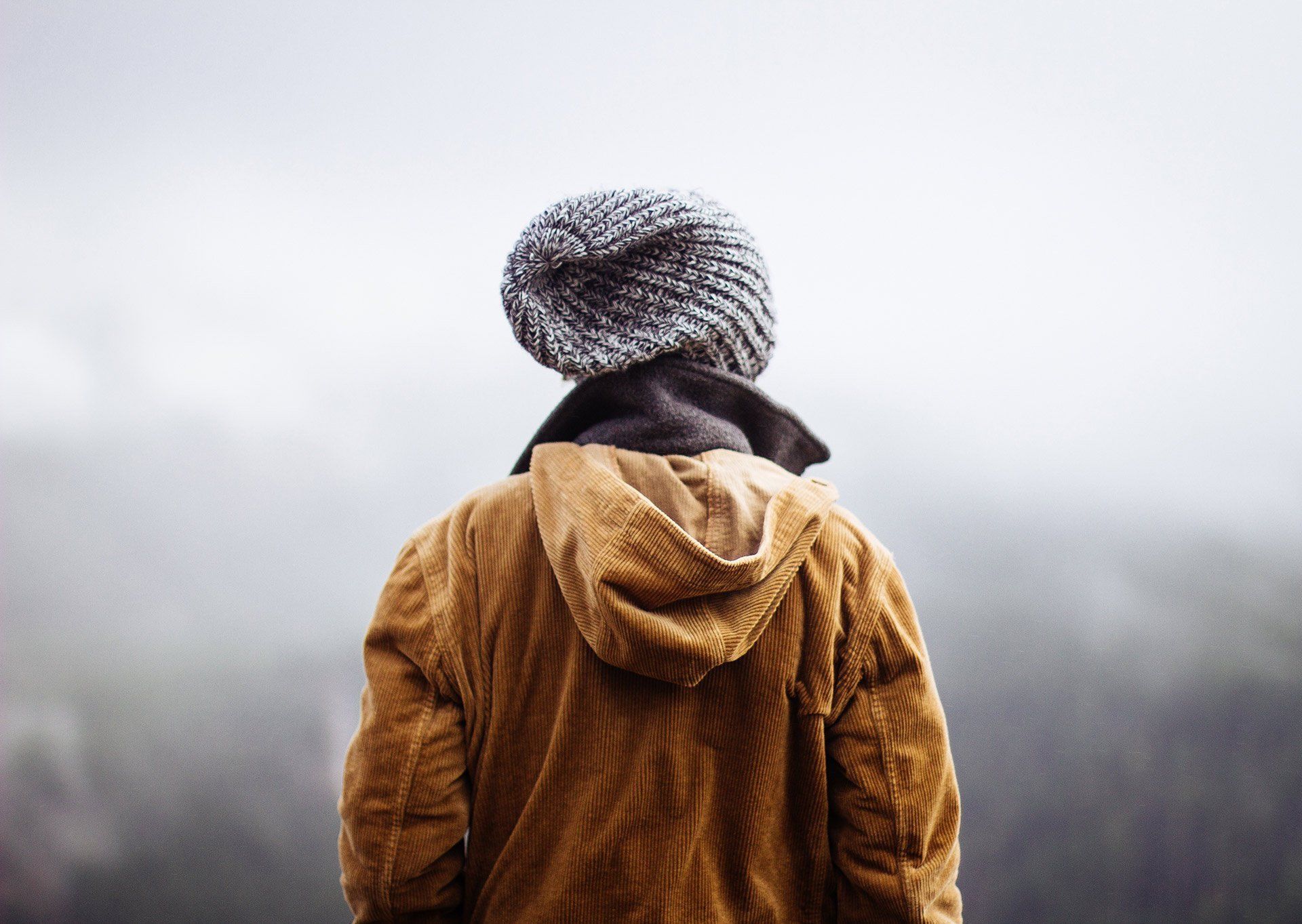 Un hombre vestido con una chaqueta con capucha y un gorro de punto está parado frente a una montaña.
