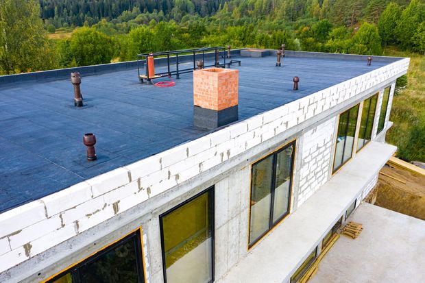 Flat roof of a modern building under construction; windows, chimney, forest in background.