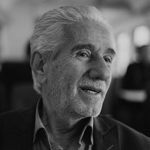 A close-up, black-and-white portrait of a person with short hair and a beard, looking slightly upward with a soft expression.