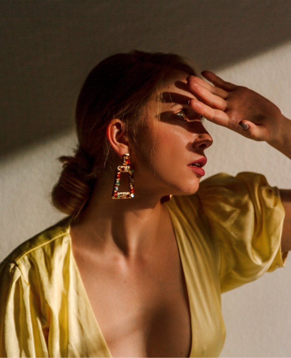 Woman in yellow dress shields eyes from sunlight, wearing earrings.