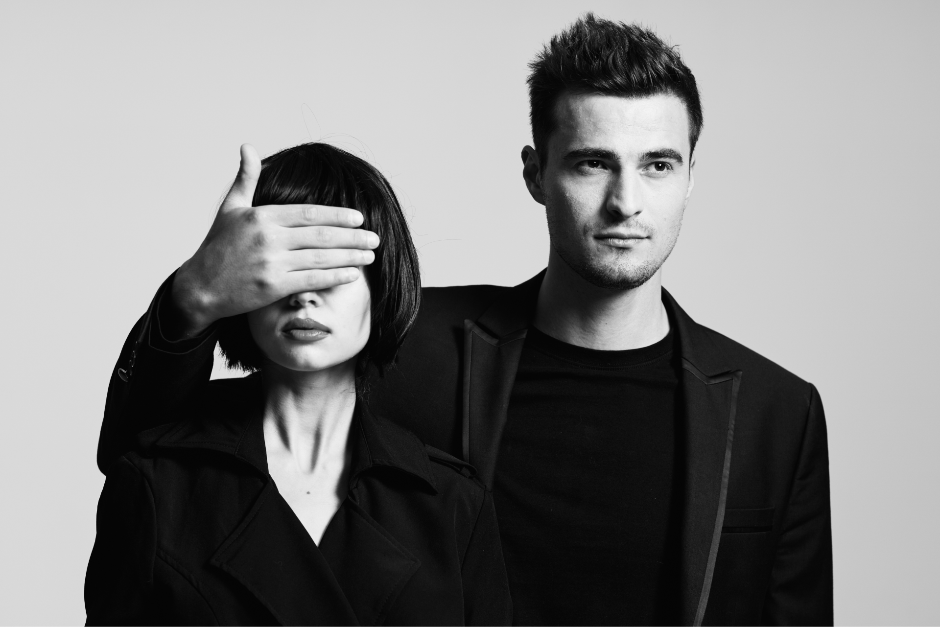 Man covering woman's eyes with his hand. Black and white, studio shot.