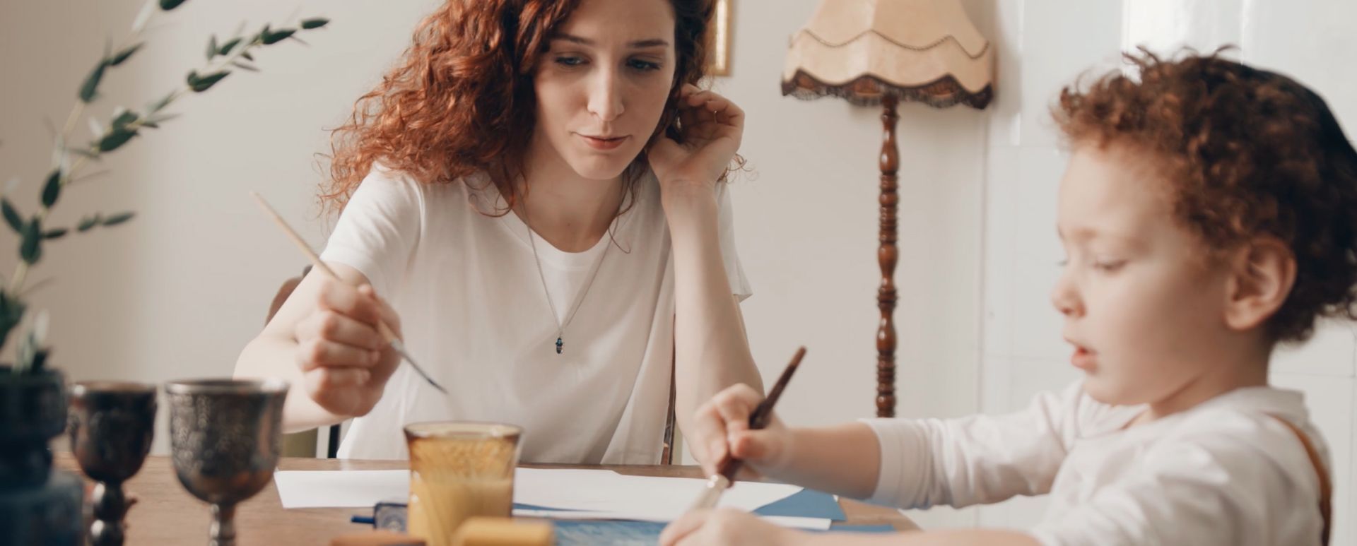 A woman and a child are sitting at a table painting with watercolors.