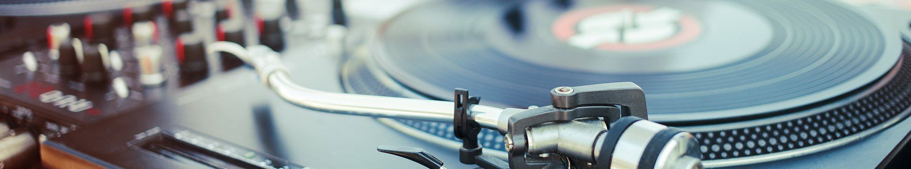 A close-up of a turntable with a spinning record. The tone arm is near the center, and the background is blurred.